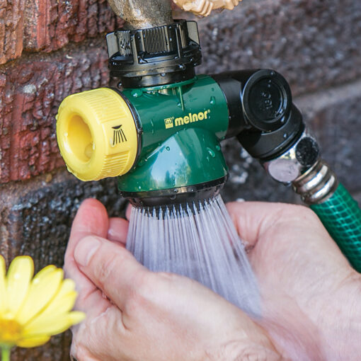 The image shows an outdoor faucet attachment with a green and yellow nozzle, a hose, and a person's hands washing under the running water.