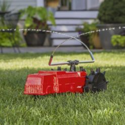 This image shows a red, toy-like sprinkler designed to resemble a fire truck, spraying water onto a lush green lawn in front of a house.