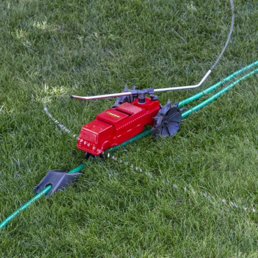 A red lawn sprinkler connected to a green hose is positioned on lush green grass, likely set to water the lawn with scattered water jets.