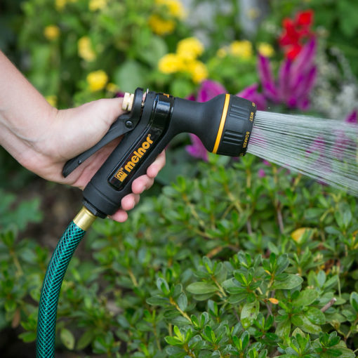 Melnor XT Metal 7-Pattern Nozzle spraying the shower spray pattern in front of colorful flowers and green bush