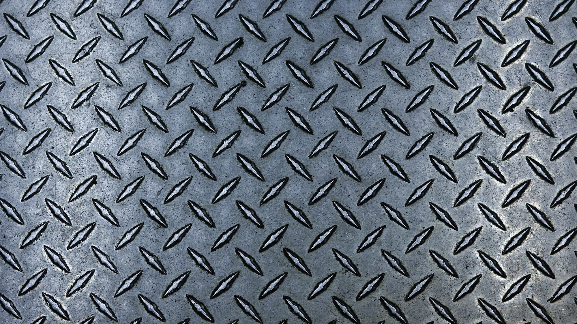 This image shows a textured metal surface with a diamond plate pattern, commonly used for its non-slip properties, featuring raised, repeating diamond shapes.