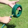 A person's hands are attaching a green, circular, plastic nozzle to a garden hose with green grass in the background, suggestive of outdoor gardening activities.