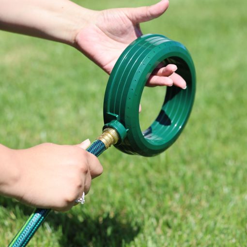 A person's hands are attaching a green, circular, plastic nozzle to a garden hose with green grass in the background, suggestive of outdoor gardening activities.