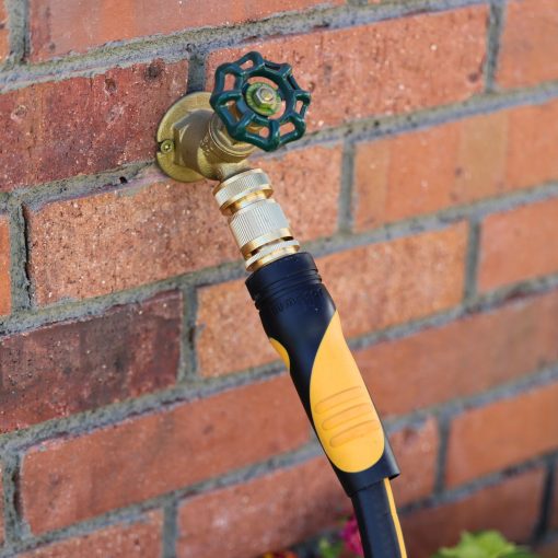 This image shows a brass outdoor faucet with a green valve handle attached to a brick wall, connected to a black and yellow garden hose.