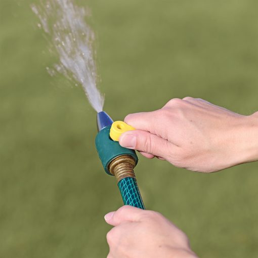 A person's hands are holding a green and blue garden hose with water spraying out against a blurred grass background. It's a close-up shot.