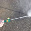 A person's hand is holding a garden hose with a nozzle, spraying a powerful jet of water onto a concrete surface, illustrating outdoor cleaning.