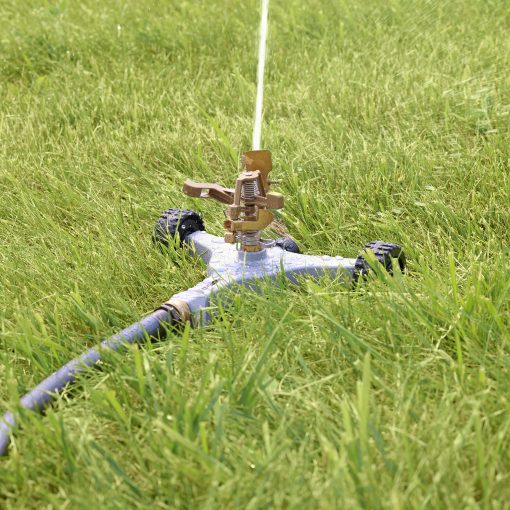 Melnor Metal Pulsating Sprinkler with Wheeled Base Spraying watering over a green lawn