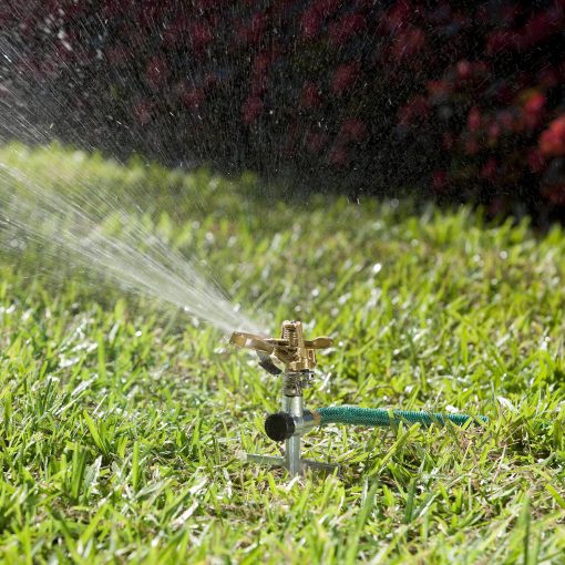 Melnor Pulsating Sprinkler on step spike spraying large stream of water on green grass