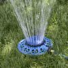 A circular blue lawn sprinkler is connected to a green hose, spraying water upwards onto green grass, providing irrigation under bright daylight conditions.