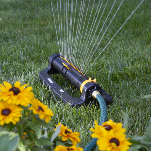 XT4200 Melnor XT 4,500 Sq. Ft. Turbo Oscillating Sprinkler with Flow Control gently spraying water over green lawn with yellow flowers