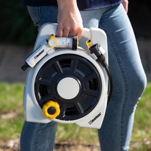 A person is holding a white and yellow electric unicycle by its handle, partly obscuring their blue jeans and casual footwear in daylight.