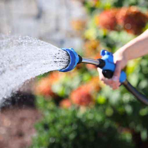 Sprout Blueberry Blue Watering Wand spraying a shower spray pattern in front of a flower bed