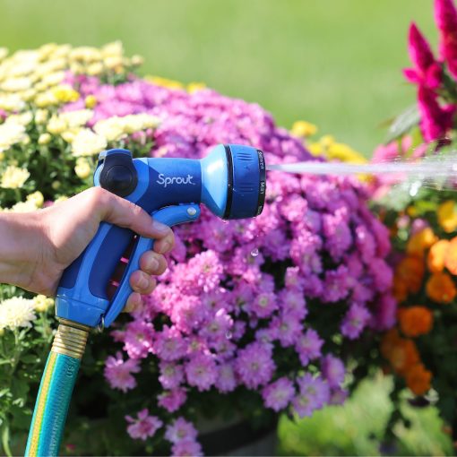 A person is watering vibrant flowers with a blue hose nozzle labeled 'Sprout'. The water spray is visible against a sunny garden backdrop.