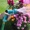 A person's hand is holding a teal garden hose nozzle, labeled 