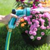 A person's hand is holding a turquoise Sprout garden hose nozzle, watering vibrant pink and orange flowers in a pot on a sunny lawn.