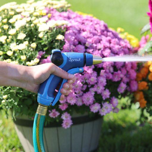 A person's hand holds a blue garden hose nozzle, labeled "Sprout," watering vibrant pink and yellow flowers in a pot under bright sunlight.