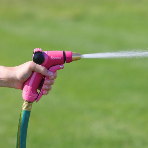 A person's hand is holding a pink garden hose nozzle, labeled "Sprout," spraying a jet of water onto a blurred green grass background.