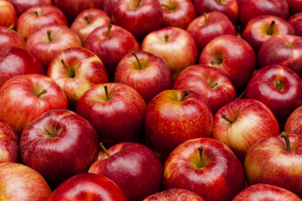 The image shows a large number of red apples closely packed together, displaying a vibrant gradient of red and yellow hues with visible stems.