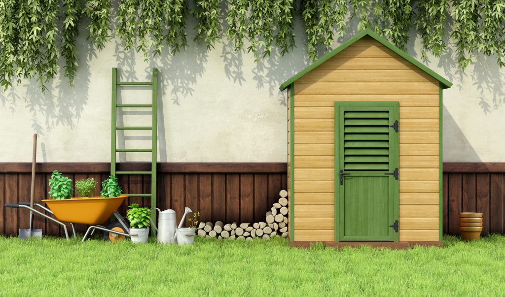 This image shows a serene garden scene with a wooden shed, green shutters, a lawn, ladder, wheelbarrow filled with soil, watering cans, and a wooden fence.