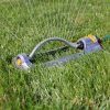 An oscillating sprinkler with a blue body and yellow fittings is lying on vibrant green grass, likely set up for watering a lawn.