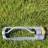 A transparent water bottle with a white flexible straw and yellow details lies in lush green grass, illuminated by bright sunlight, appearing unused.