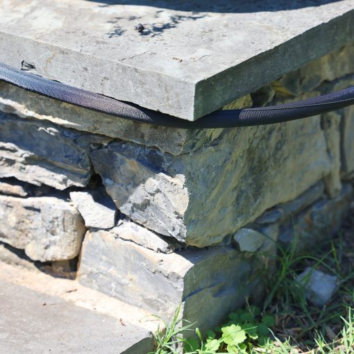 Melnor Heavy-Duty fabric hose being pulled around a rock wall