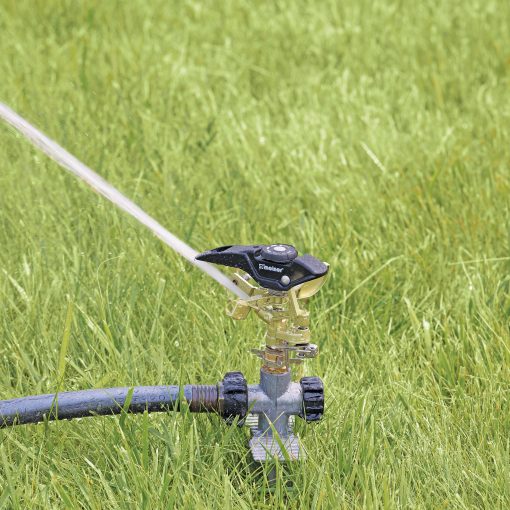 An oscillating sprinkler is attached to a hose on a lush green lawn, spraying water to irrigate the grass under bright daylight.